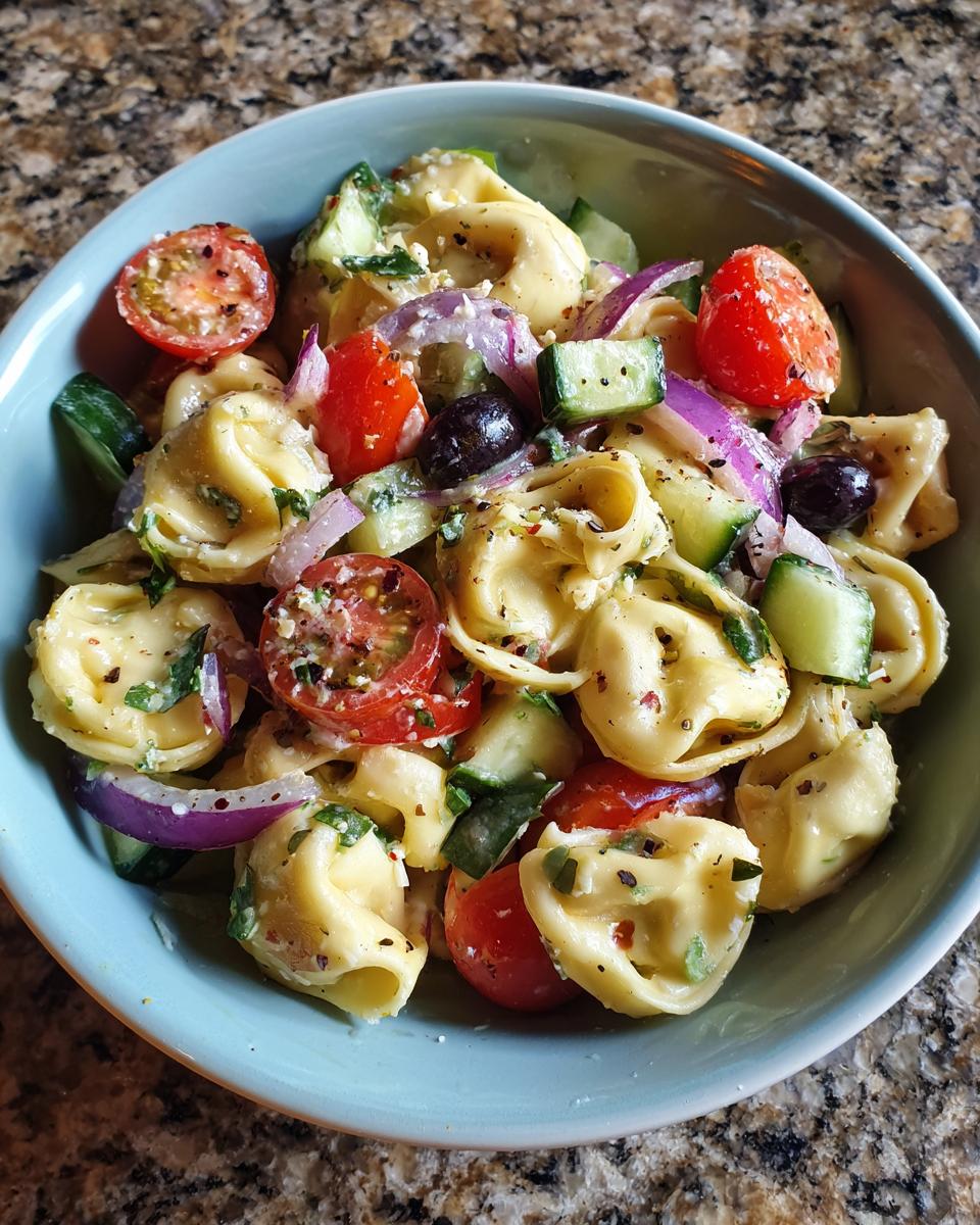 Close-up of a bowl of pasta salad tortellini with tomatoes, cucumbers, and olives.