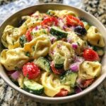 Close-up of a bowl of pasta salad tortellini with tomatoes, cucumbers, and red onion.