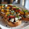 Close-up of Peach Burrata Bruschetta on toasted bread, topped with peaches, basil, and balsamic glaze.