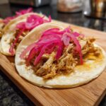 Close-up of Pulled Chicken Tacos with Pickled Red Onion on a wooden board.