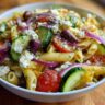 Close-up of a bowl of quick mediterranean pasta salad with tomatoes, olives, cucumber, and feta.