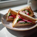 Close-up of three triangle-cut Radish & Butter Tea Sandwiches on a plate, with radishes and greens.
