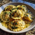 Close-up of a bowl of Ricotta & Lemon Ravioli with Brown Butter, garnished with herbs and lemon zest.
