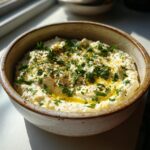 Close-up of a bowl of Roasted Garlic & White Bean Dip, garnished with herbs and olive oil.