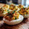 Close-up of Spicy Elote Deviled Eggs, garnished with chives and paprika, on a wooden board.