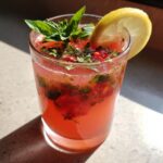 A glass of vibrant Strawberry Basil Lemonade garnished with basil and a lemon slice.