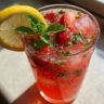 A tall glass of Strawberry Basil Lemonade with fresh strawberries, basil, and a lemon slice.