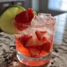 Close-up of a Strawberry Lime Vodka Smash cocktail with fresh strawberries and lime.