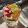 Close-up of a refreshing summer vodka cocktail with ice, strawberries, lime, and orange slices.