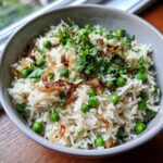 Close-up of Sweet Pea & Shallot Pulao in a bowl, garnished with herbs and fried shallots.