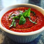 Close-up of Tomato Basil Gazpacho in a white bowl, garnished with fresh basil and olive oil.