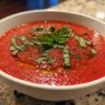 Close-up of a bowl of Tomato Basil Gazpacho, garnished with fresh basil leaves and oil.