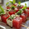 Close-up of Watermelon Feta Skewers on a white plate, garnished with fresh mint and balsamic glaze.