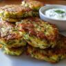 Stack of golden-brown Zucchini Fritters with a side of creamy Tzatziki sauce, perfect for dipping.